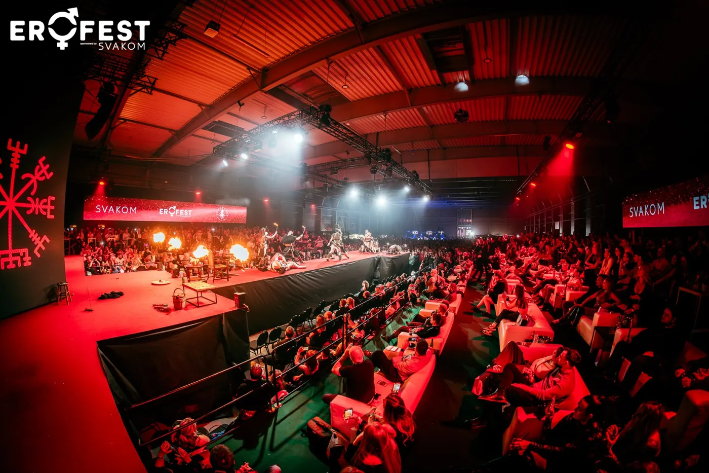 Zaplněná hala EroFestu v rudém světle reflektorů, diváci u stolů před hlavní stage
